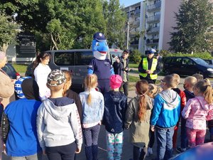 Policjanci i Polfinek podczas prelekcji dla dzieci przed szkołą.