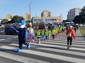 Dzieci podczas przechodzenia przez przejście dla pieszych w towarzystwie Polfinka i policjantów.