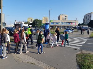 Grupa dzieci wchodzi na przejście dla pieszych. Przed nimi idzie Polfinek.