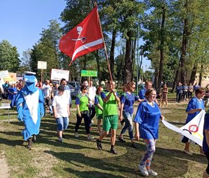 Defilada uczestników olimpiady. Wśród nich idzie maskotka Polfinek.