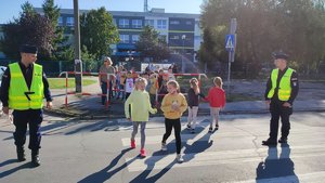 Dzieci przechodzą w parach przez przejście dla pieszych pod okiem policjantów.