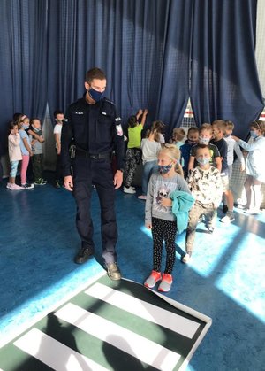 Policjant i dzieci stoją przed matą imitującą przejście dla pieszych.