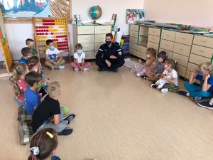 Policjant rozmawia z dziećmi. Wszyscy siedzą w okręgu na podłodze w klasie szkolnej.
