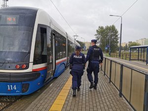 Policjanci na przystanku tramwajowym. W tle stojący tramwaj.