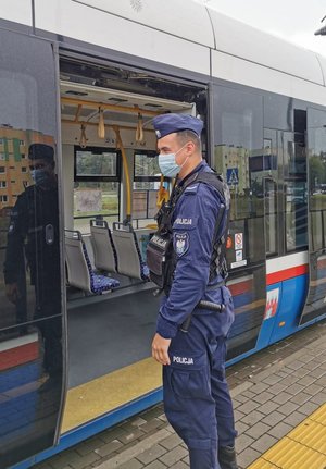 Policjant stoi obok tramwaju i patrzy do jego środka.