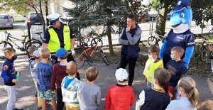 Policjant, Polfinek oraz pracownik Word-u rozmawiają z dziećmi na świeżym powietrzu.