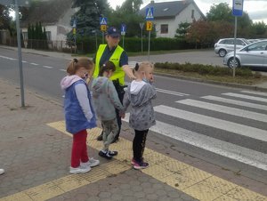 Policjantka stoi z kilkoma uczniami przy przejściu dla pieszych.