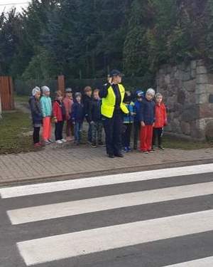 Policjantka stoi z grupą uczniów przy przejściu dla pieszych.