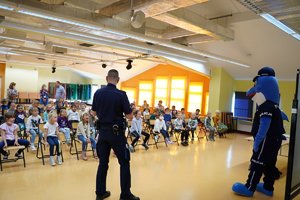 Policjant i Polfinek prowadzą zajęcia z uczniami w sali szkolnej.