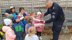 Policjant zakłada dzieciom na ręce opaski odblaskowe.