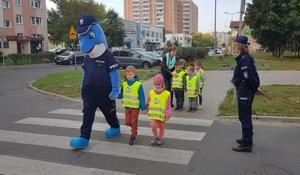 Polfinek przeprowadza dzieci przez przejście dla pieszych pod okiem policjantki.