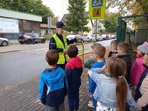 Policjantka rozmawia z uczniami w rejonie przejścia dla pieszych.