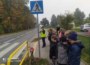 policjantka pokazuje dzieciom przed przejściem dla pieszych, jak należy zachowywać się przed przejściem