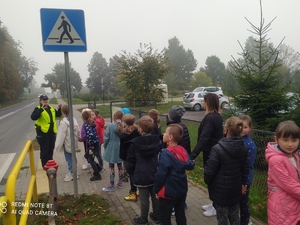 policjantka pokazuje dzieciom przed przejściem dla pieszych, jak należy zachowywać się przed przejściem