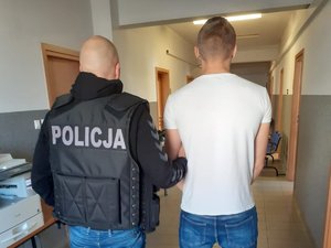 Policjant z zatrzymanym na korytarzu budynku.