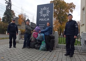 Policjanci i tata Szymka stoją przed Komendą Miejską Policji w Bydgoszczy przy workach z nakrętkami.