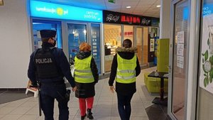 Policjant i pracownicy sanepidu idą korytarzem galerii handlowej.