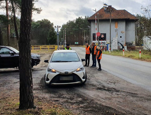 Policjant kontroluje samochód osobowy marki Toyota. Przyglądają się temu pracownicy kolei.