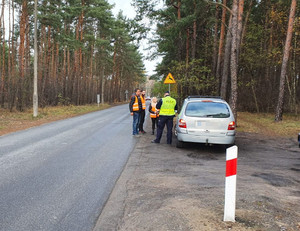 Policjant stoi przy kontrolowanym samochodzie marki Renault. Przyglądają się temu pracownicy kolei.