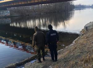 Policjant i strażnik rybacki kontrolują nabrzeże rzeki.