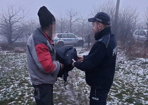 Policjant przekazuje kurtko-śpiwór bezdomnemu mężczyźnie.