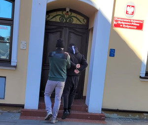 Policjant z zatrzymanym na schodach budynku prokuratury.