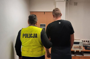 Pomieszczenie.- policjant stoi tyłem z drugim sprawcą.