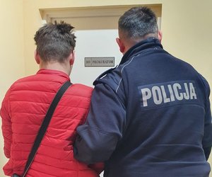 Policjant prowadzi zatrzymanego do pokoju prokuratora.