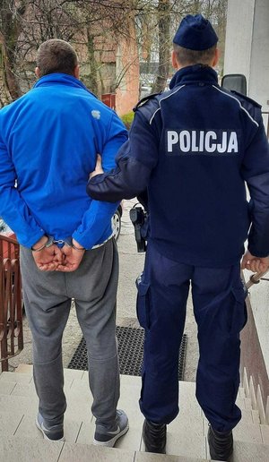 umundurowany policjant trzyma skutego kajdankami zatrzymanego mężczyznę