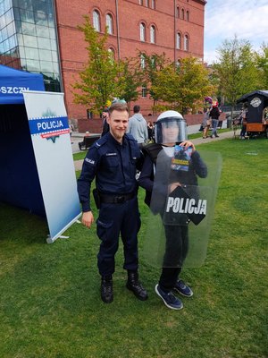 Policjant stoi obok nastolatka trzymającego policyjną tarczę ochronną.