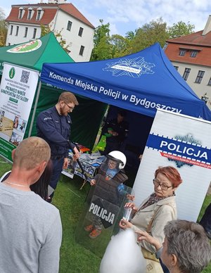 Policjant, dzieci i osoby dorosłe stoją przed namiotem policyjnym.