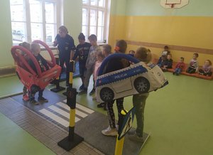 Dzieci ćwiczą z policjantką bezpieczne poruszanie się na drodze przy pomocy &quot;Autochodzika&quot;.