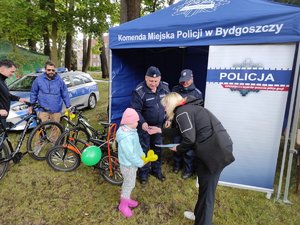 Dziecko, dorośli oraz policjanci przy stoisku policyjnym.