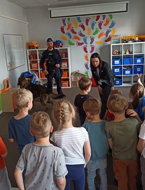 Policjant z psem służbowym stoi przed dziećmi.