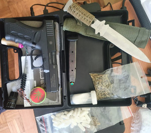 w pudełku leży pistolet, obok jest magazynek z amunicją, nóż, woreczki i plastikowe pudełko z rożnymi substancjami oraz dwa woreczki z zielonym suszem