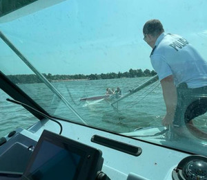 Widok ze środka łodzi. Policjant stoi na policyjnej łodzi motorowej i udziela pomocy osobom na łodzi.