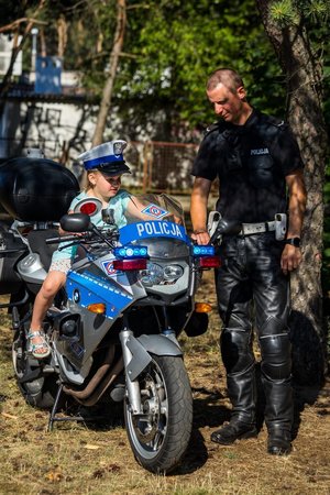 dziecko siedzi na motocyklu policyjnym. Przy nim stoi policjant.