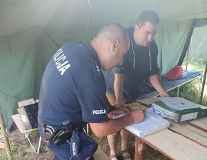 Policjant stojąc wypisuje dokument. Obok stoi mężczyzna.