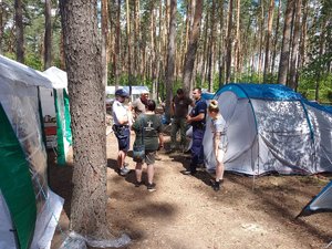 Policjant podczas rozmowy z obozowiczami stoją wśród drzew i namiotów.