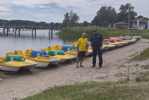 policjant i mężczyzna stojący na tle jeziora i rowerów wodnych