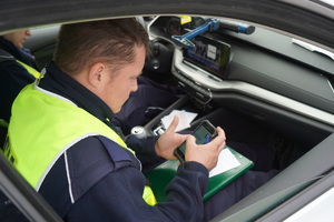 Policjant siedzi w radiowozie i sporządza dokumentację.