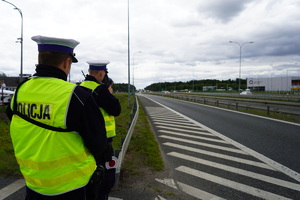 Policjant mierzy prędkość laserowym miernikiem prędkości. Za nim stoi drugi policjant.