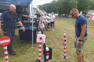 mężczyzn idzie z założonymi alkogoglami. Obok przygląda się policjant