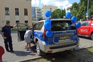 policjant otwiera drzwi od radiowozu i pokazuje dzieciom pojazd