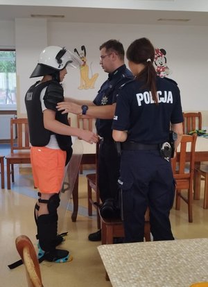 Policjanci stoją z nastolatkiem, który ma założone umundurowanie bojowe.