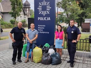 Policjanci i tata chłopca przy zebranych nakrętkach przez budynkiem komendy.