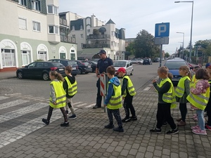 Dzieci wraz z policjantem przy przejściu dla pieszych.