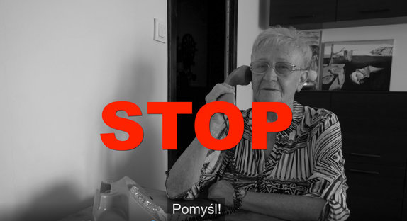 kadr z filmu, na którym seniorka siedząca przy stole rozmawia przez telefon, na kadrze tym widoczny napis STOP