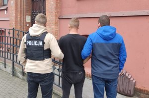 Policjanci idą z zatrzymanym do budynku sądu.