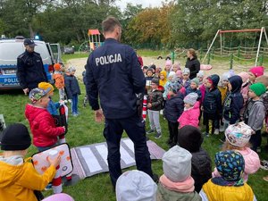 Dzieci i policjanci stoją przy macie imitującej przejście dla pieszych.